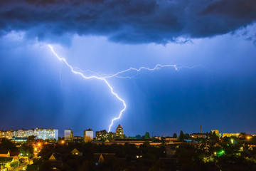 Lightning over the city in the night sky strikes the roof of the house