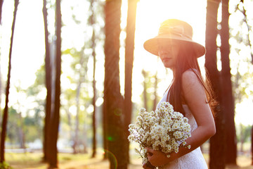 Female in white holding a white flower Cutter, side view in pine forest. with copy space.