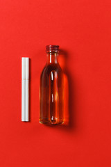 Two white cigarettes, bottle with alcohol cognac, whiskey on red background. Health, choice, healthy lifestyle concept. Copy space for advertisement. With place for text.