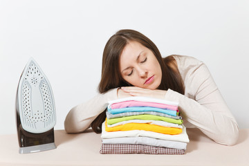 Young tired pretty housewife in light casual clothes fell asleep on family clothing on ironing board with iron. Woman isolated on white background. Housekeeping concept. Copy space for advertisement.