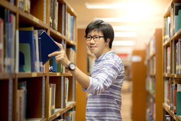 Young Asian man university student choosing book in library, education research and self learning in university life concepts