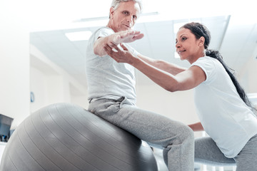 Very good. Determined old wrinkled grey-haired man sitting on a ball for exercises and a pretty...