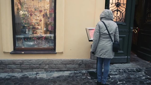 Young woman reading menu outdoors in front of the restaurant and comes inside. Woman looking at restaurant outdoor menu on the street.