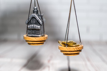 Stack of coins and a small house on the scales. The concept of choice, cash savings and purchase of real estate.