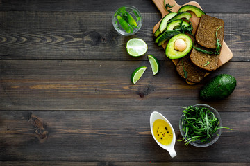 Fototapeta na wymiar Breakfast for safety weight loss. Avocado toast with rye bread, lime, olive oil and greens on dark wooden background top view space for text
