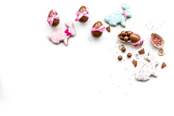 Sweets for Easter table. Chocolate eggs near cookies in shape of Easter bunny on white background top view copy space