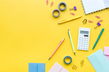 Scattered stationery on student's desk. Yellow background top view copy space