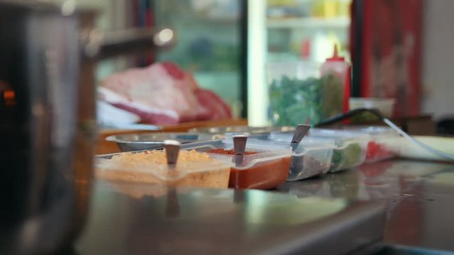 Commercial kitchen, meat and spices on the table, pot on the stove
