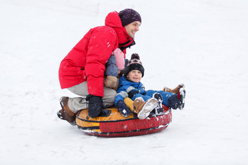 Fototapeta na wymiar Picture of father, son, daughters riding tubing in winter park