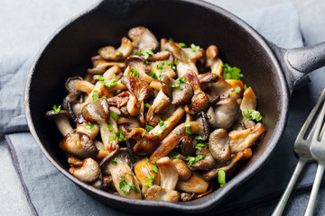 Fried mushrooms with fresh herbs in black cast iron pan.