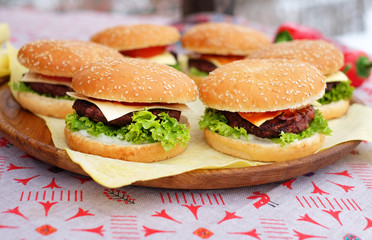 Beef and cheese burgers with green salad and sauce lying on a wooden plate at street food festival.