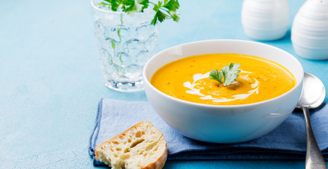 Pumpkin and carrot soup with cream and parsley on blue stone background. Copy space.