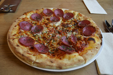 A yummy but unhealthy fast food pizza with salami, cheese, tomato sauce, herbs and crispy crust