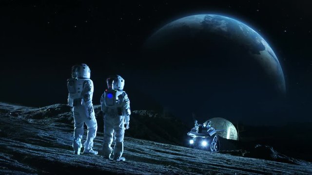Two Astronauts in Space Suits Stand on the Moon Looking at the Beautiful Earth. In the Background Lunar Base with Geodesic Dome. Moon Colonization. Shot on RED EPIC-W 8K Helium Cinema Camera.