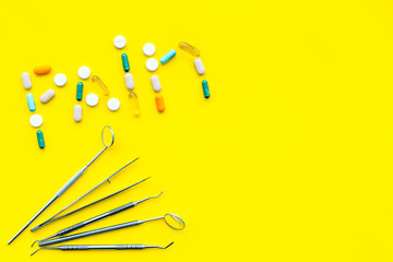 Toothache, dental pain. Fear of dental treatment. Word pain lined with pills near dentist tools. Yellow background top view copy space