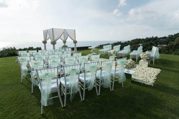 Wedding arch decorated with white and green flowers outdoors. Beautiful wedding set up. Wedding ceremony on green lawn in the terrace. Part of the festive decor, floral arrangement.