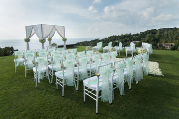 Wedding arch decorated with white and green flowers outdoors. Beautiful wedding set up. Wedding ceremony on green lawn in the terrace. Part of the festive decor, floral arrangement.