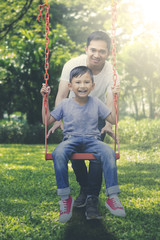 Happy father and son playing with a swing at park