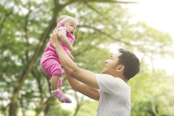 Father lifting daughter with blur tree background