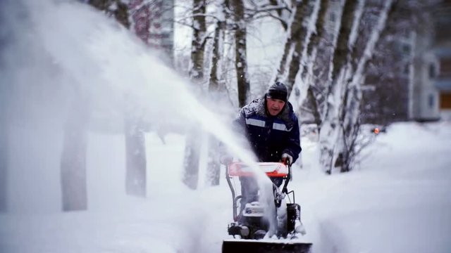 The janitor clears the track with a snowplow in the courtyard of an apartment building.