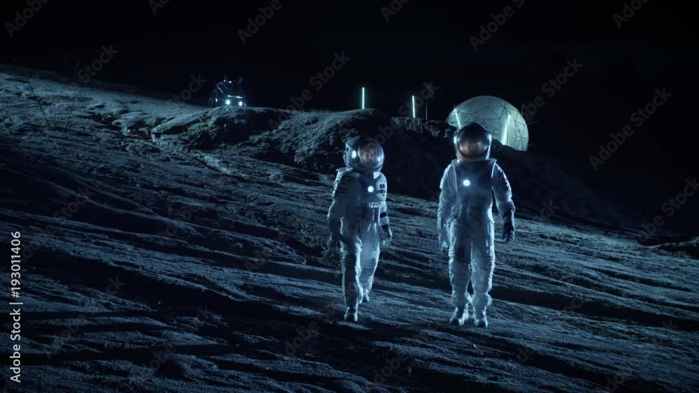 Wall mural two astronauts in space suits walk on the alien planet looking at the sky. in the background base wi
