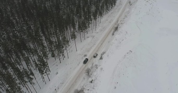 Car driving on winter country road in snowy forest. Aerial footage.