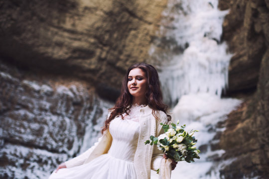 Sexy bride holding a bouquet of flowers from roses on the background of a glacier