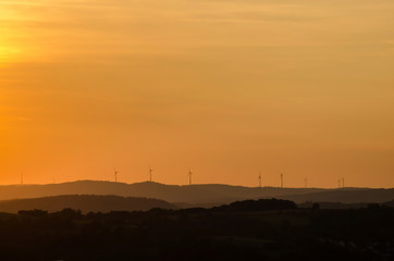 Fototapeta na wymiar Sunset over Gladenbacher windpark. Silhouettes of wind generators on sunset background. Landscape.