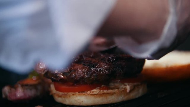 Chef preparing the burger, frying the bun on the grill, putting the tomatoes, meat and sauce