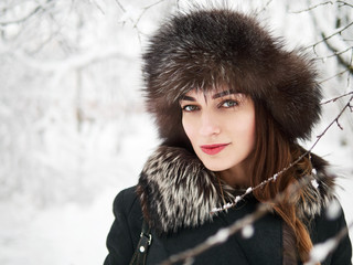 Adorable happy young brunette woman in fur hat having fun snowy winter park forest in nature