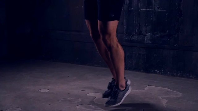 Tilt up of determinate sportsman working out with jumping rope, slow motion