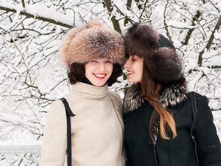 Adorable happy young brunette women girlfriends in fur hats having fun snowy winter park forest in...