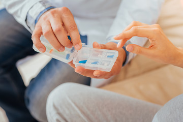 Take it please. Pleasant skilled responsible doctor sitting near a woman holding and giving pills for her.