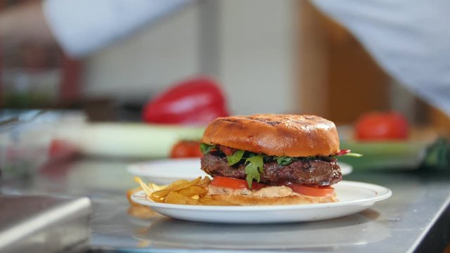 Chef serves a burger by adding potato chips on a plate