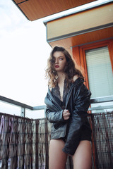 Young sexy woman in a jacket fur coat and lingerie standing on balcony