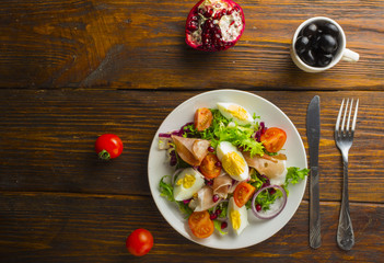 Fresh salad with mixed greens and cherry tomato in bowl on wooden background