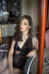 Fototapeta na wymiar Young sexy woman in black lingerie poses outside the window