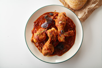 Chicken legs cooked in italian cacciatore style with tomato sauce and fresh basil on white table
