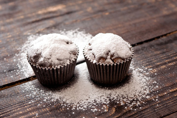 chocolate muffins sprinkled with powdered sugar on a dark wooden table