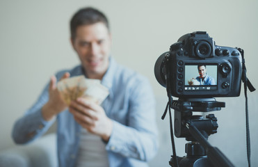 Man making video blog about money earning. Focus on camera.