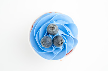 Cupcake red velvet with blue whipped cream decorated with blueberry on white background. Picture for a menu or a confectionery catalog. Top view.