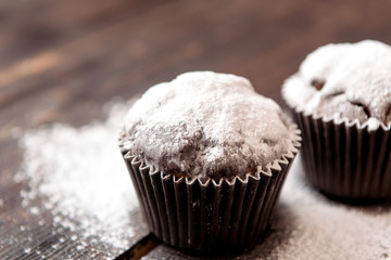 chocolate muffins sprinkled with powdered sugar on a dark wooden table