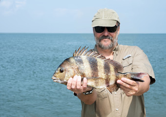 A fisherman is holding a fish  Southern sheeps head (Archosargus probatocephalus)  against the sea