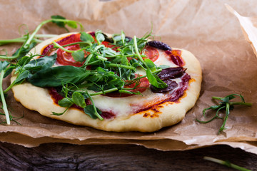 Homemade pizza with tomatoes and sprouts topping on rustic table