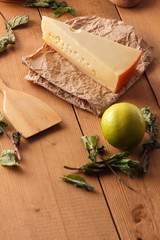 Hard cheese, lemon, lime and mint on a wooden background, wooden spatula, mint leaves with cheese and holes, rustic style, parchment cheese, healthy food, vegan