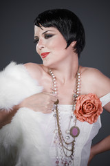Brunette girl with short hair, French mane in the style of the 20s. She wears white fur coat and...