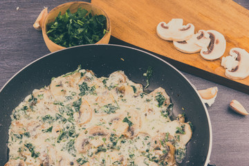 Creamy sauce with mushrooms and greens in a frying pan