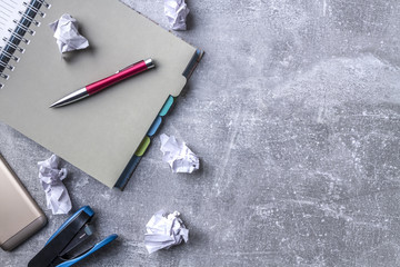 Gray desk top with notebook, smartphone, paper stapler and crumpled sheets of paper