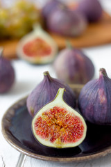 Half of fig fruit on a brown ceramic plate over white wooden table.