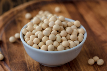 Organic soybeans at white ceramic bowl over wooden table.